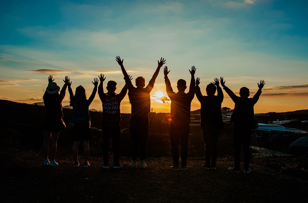 Image of a group of people as silhouettes in front of the rising sun clasping hands